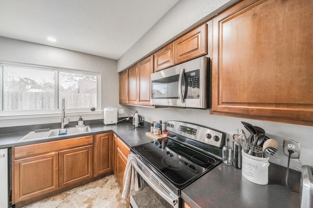 kitchen featuring stainless steel appliances, brown cabinetry, dark countertops, and a sink