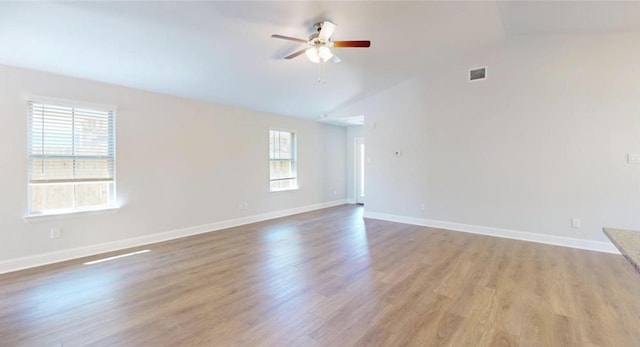 unfurnished room with visible vents, light wood-style floors, a ceiling fan, vaulted ceiling, and baseboards