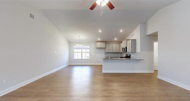 unfurnished living room featuring light wood-type flooring, vaulted ceiling, baseboards, and ceiling fan with notable chandelier