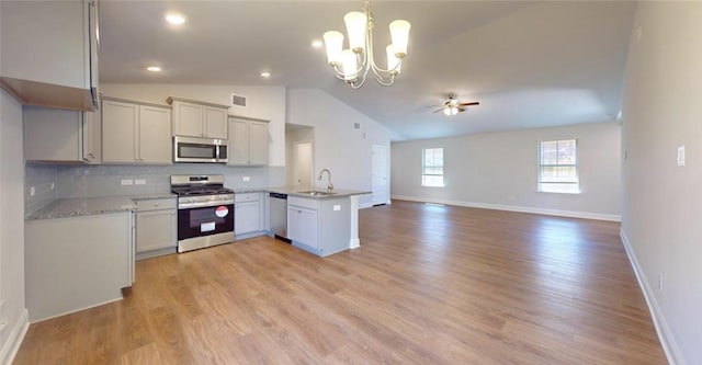 kitchen featuring a peninsula, a sink, open floor plan, appliances with stainless steel finishes, and decorative light fixtures