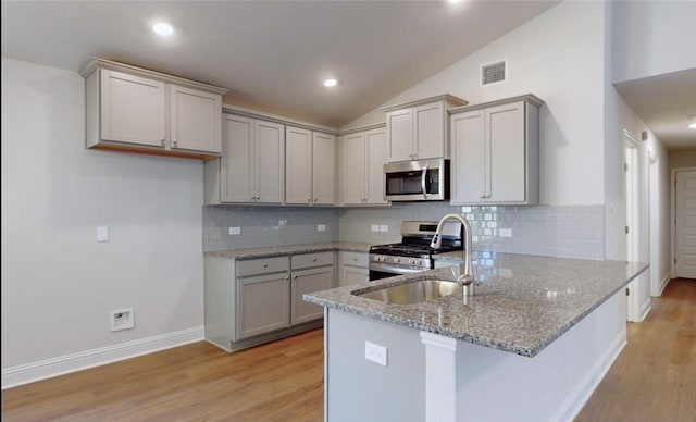 kitchen with appliances with stainless steel finishes, a peninsula, light stone countertops, vaulted ceiling, and a sink