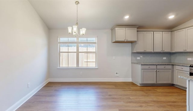 kitchen featuring lofted ceiling, gray cabinets, decorative backsplash, a chandelier, and light wood-type flooring