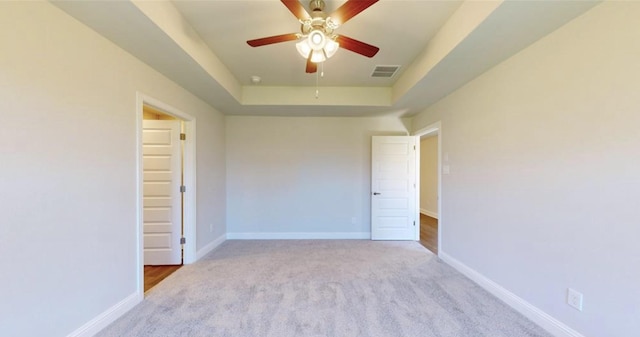 unfurnished room with light carpet, a ceiling fan, visible vents, baseboards, and a tray ceiling