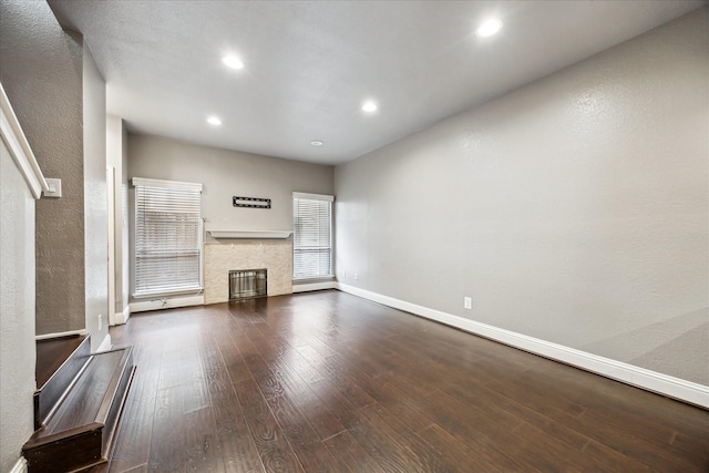 unfurnished living room with dark wood-style flooring, recessed lighting, a glass covered fireplace, and baseboards