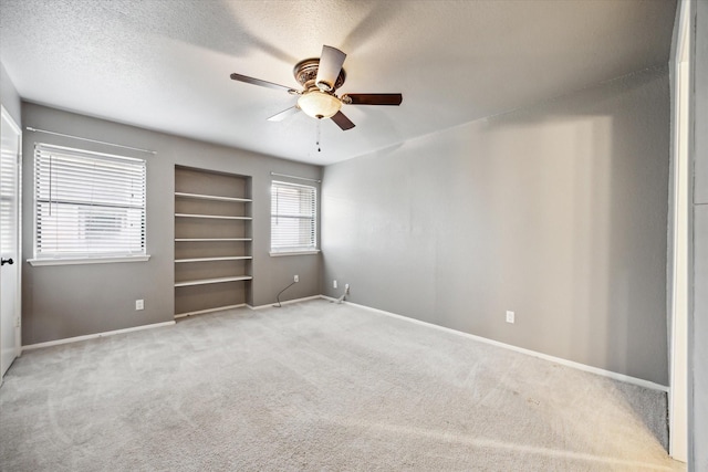 spare room featuring a textured ceiling, light colored carpet, a ceiling fan, baseboards, and built in features