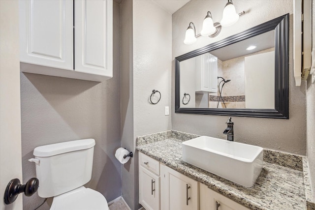 bathroom featuring toilet, a textured wall, and vanity