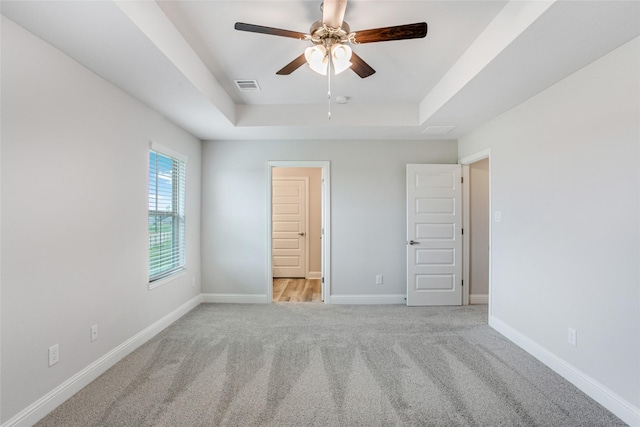 unfurnished bedroom with light carpet, a ceiling fan, visible vents, baseboards, and a raised ceiling