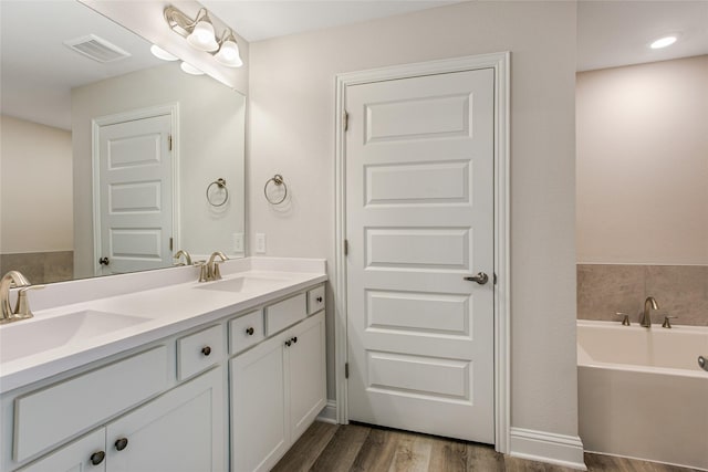 full bathroom with double vanity, a garden tub, a sink, and wood finished floors