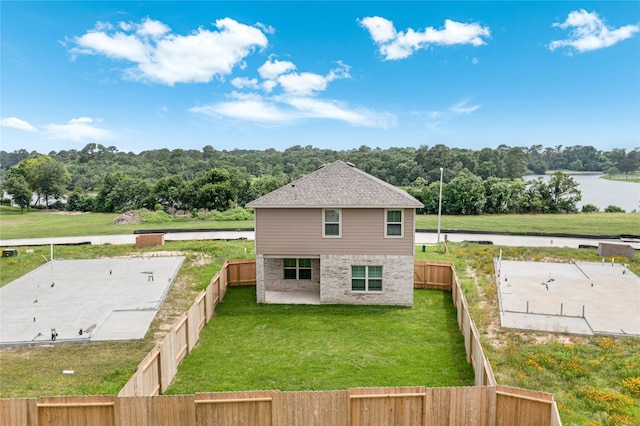 back of property with brick siding, a shingled roof, a lawn, a fenced backyard, and a forest view