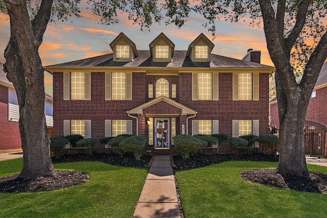 colonial inspired home featuring a yard and brick siding