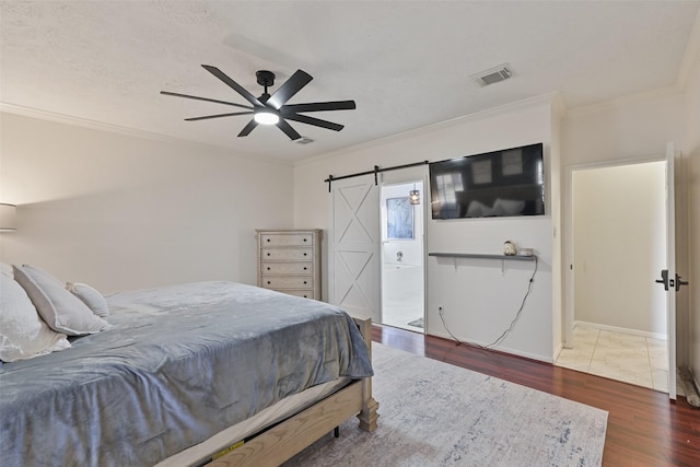 bedroom with wood finished floors, visible vents, ceiling fan, ornamental molding, and a barn door