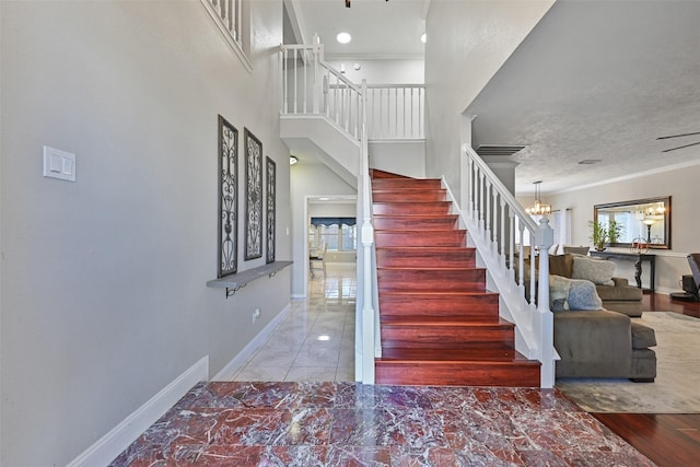 stairs with baseboards, a notable chandelier, ornamental molding, and a towering ceiling