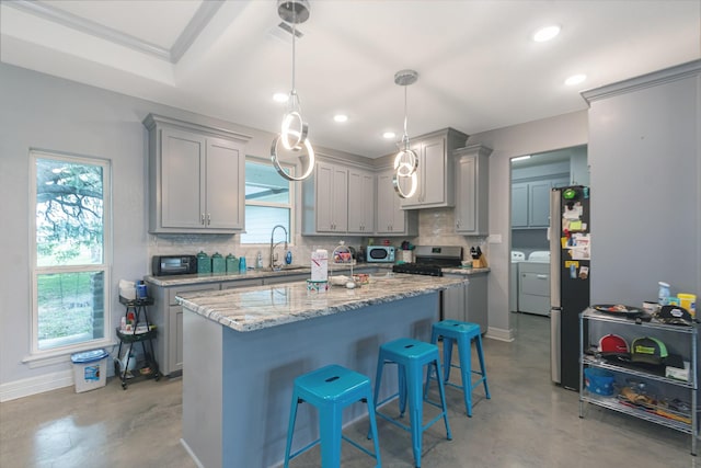 kitchen featuring decorative backsplash, stainless steel appliances, concrete flooring, gray cabinets, and washer and dryer