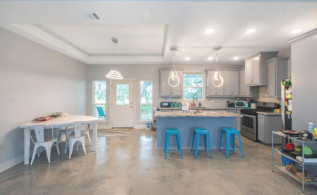 kitchen featuring a tray ceiling, pendant lighting, gray cabinets, stainless steel gas range oven, and a kitchen bar