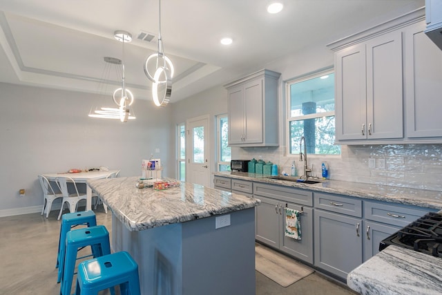 kitchen with a raised ceiling, a kitchen island, a breakfast bar, hanging light fixtures, and a sink