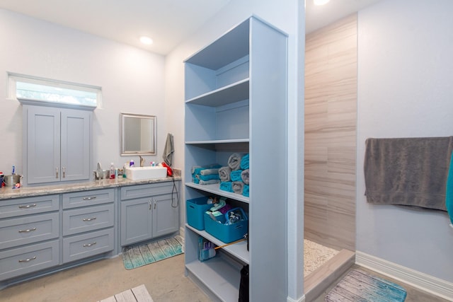 full bathroom featuring double vanity, baseboards, a sink, and tiled shower