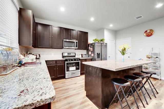 kitchen featuring stainless steel appliances, light wood-style floors, a kitchen island, and a kitchen breakfast bar