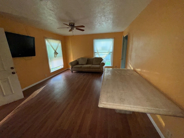 unfurnished living room with dark wood finished floors, a textured ceiling, baseboards, and ceiling fan