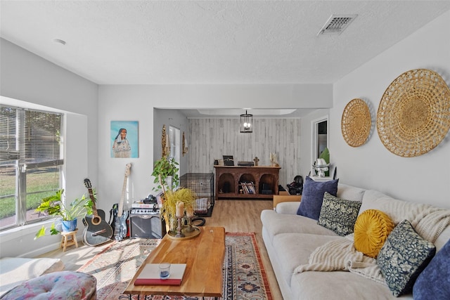 living room featuring visible vents, light wood-style flooring, an accent wall, a textured ceiling, and wood walls