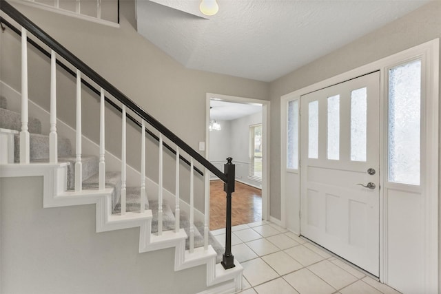 foyer featuring light tile patterned floors, a textured ceiling, stairs, and baseboards