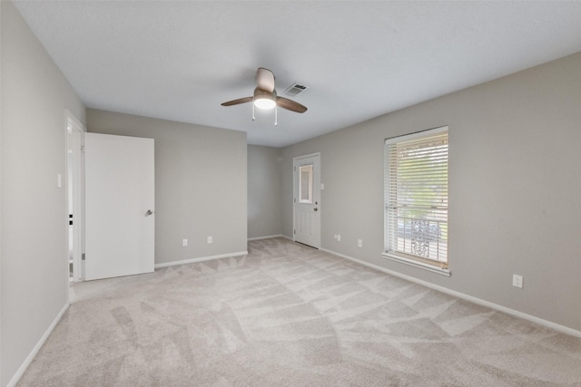 spare room featuring light carpet, ceiling fan, visible vents, and baseboards