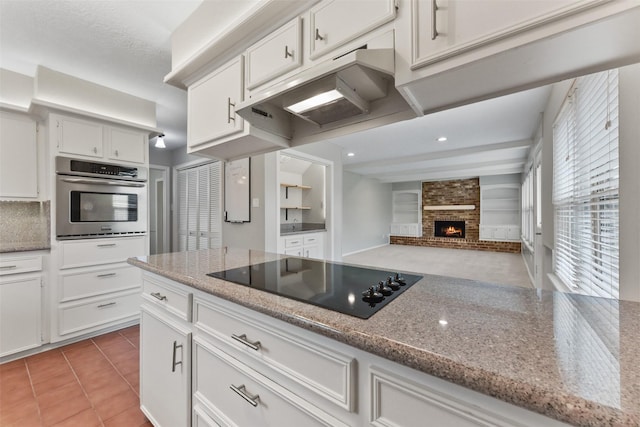 kitchen featuring white cabinets, light stone counters, black electric cooktop, under cabinet range hood, and stainless steel oven