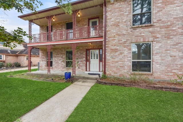 view of front facade featuring brick siding, a front lawn, covered porch, and a balcony