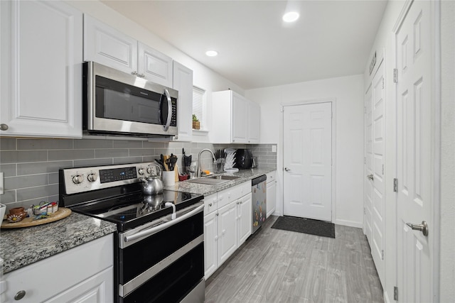 kitchen with stainless steel appliances, tasteful backsplash, white cabinetry, a sink, and light stone countertops