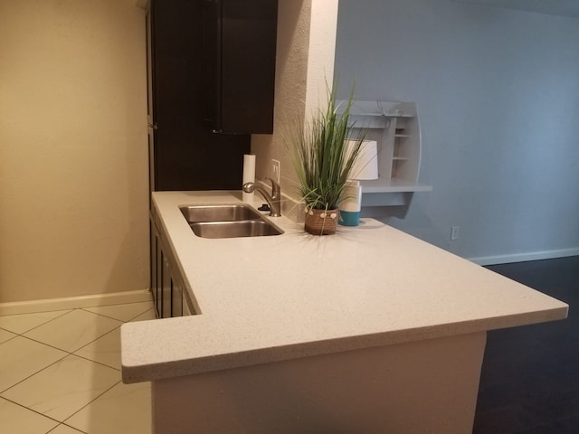 kitchen featuring a peninsula, baseboards, light countertops, and a sink