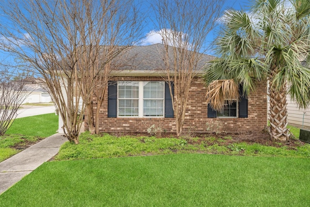 view of side of property with roof with shingles, brick siding, and a lawn