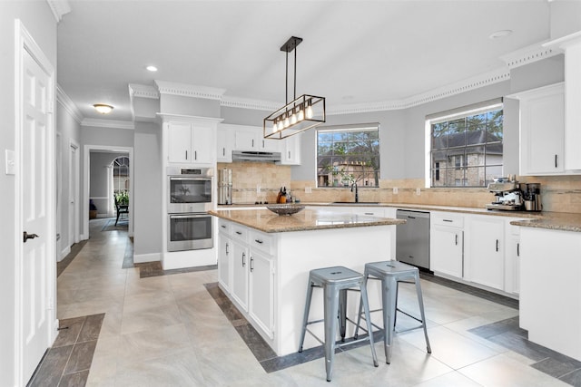 8014 Northbridge Cir, Spring, TX 77379 - kitchen with stainless steel appliances, a sink, a center island, under cabinet range hood, and ornamental molding
