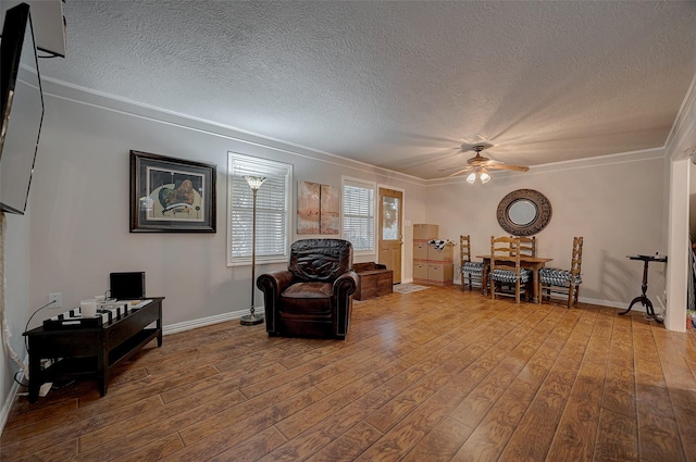 sitting room with ceiling fan, a textured ceiling, wood finished floors, baseboards, and ornamental molding