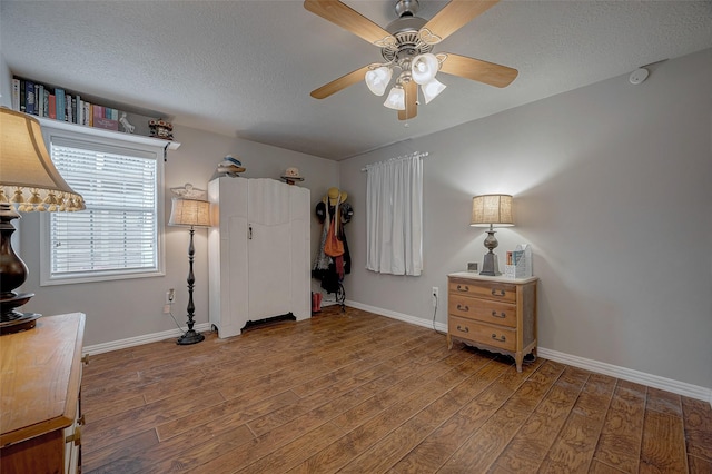 bedroom featuring ceiling fan, a textured ceiling, baseboards, and wood finished floors