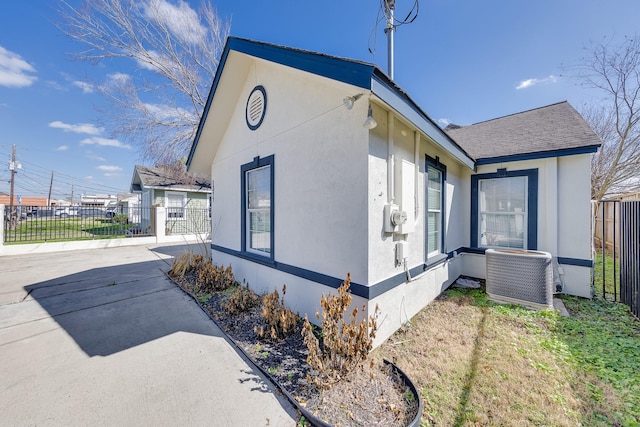 view of property exterior with stucco siding, central air condition unit, a shingled roof, and fence