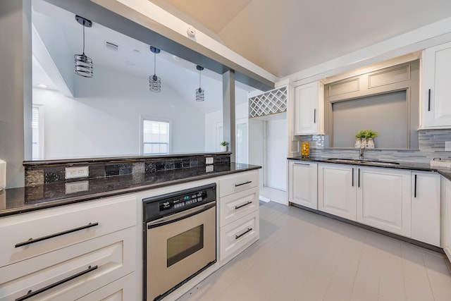 kitchen featuring oven, a sink, white cabinets, vaulted ceiling, and pendant lighting