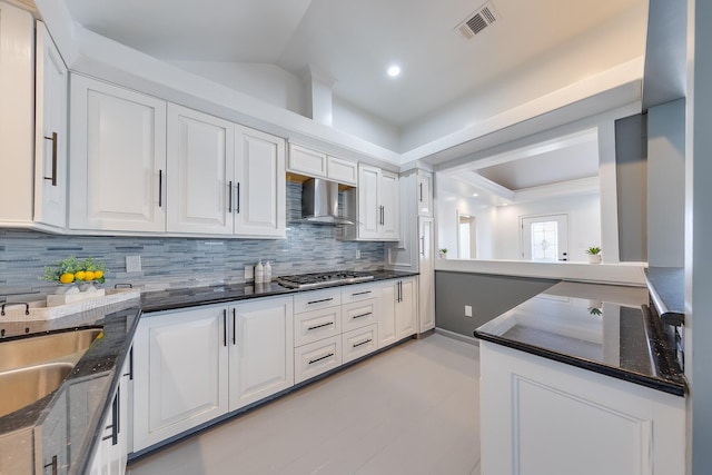 kitchen featuring visible vents, decorative backsplash, white cabinetry, wall chimney exhaust hood, and a sink