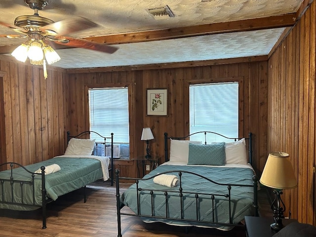 bedroom with wooden walls, a textured ceiling, visible vents, beam ceiling, and wood finished floors