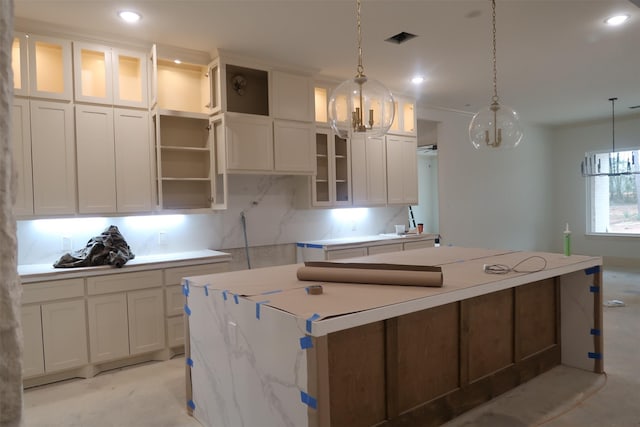 kitchen featuring a kitchen island, glass insert cabinets, white cabinets, and decorative light fixtures