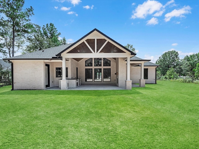 back of house with a shingled roof, brick siding, a patio, and a lawn