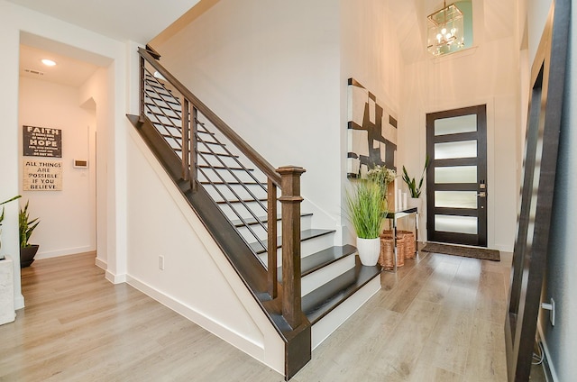 foyer entrance with light wood finished floors, stairway, baseboards, and an inviting chandelier