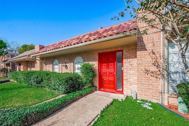 view of exterior entry with a yard, a tile roof, and brick siding