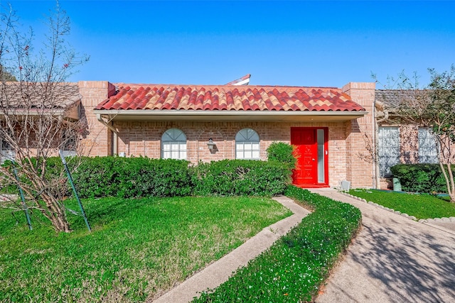 view of front facade with brick siding, a tile roof, and a front yard