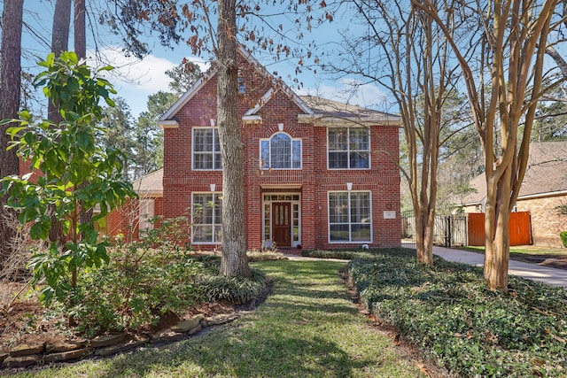 view of front facade featuring brick siding, a front yard, and fence