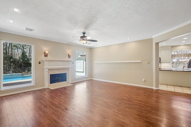 unfurnished living room featuring hardwood / wood-style floors, a ceiling fan, baseboards, a fireplace with flush hearth, and a textured ceiling