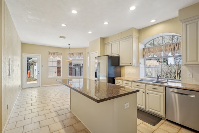 kitchen featuring tasteful backsplash, a kitchen island, dark stone counters, appliances with stainless steel finishes, and a sink