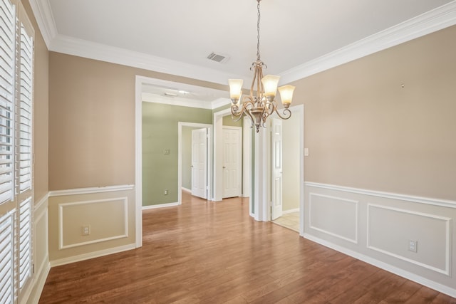 unfurnished dining area featuring visible vents, a notable chandelier, ornamental molding, wood finished floors, and a decorative wall