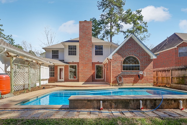 back of property with a fenced in pool, fence, brick siding, and a chimney