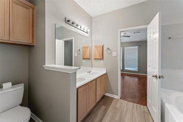 bathroom featuring toilet, a sink, wood finished floors, double vanity, and a bath