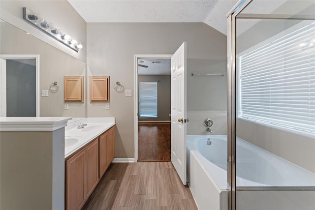 full bath with a textured ceiling, wood finished floors, double vanity, a bath, and vaulted ceiling