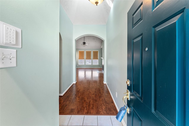 tiled foyer with baseboards, arched walkways, and a textured ceiling